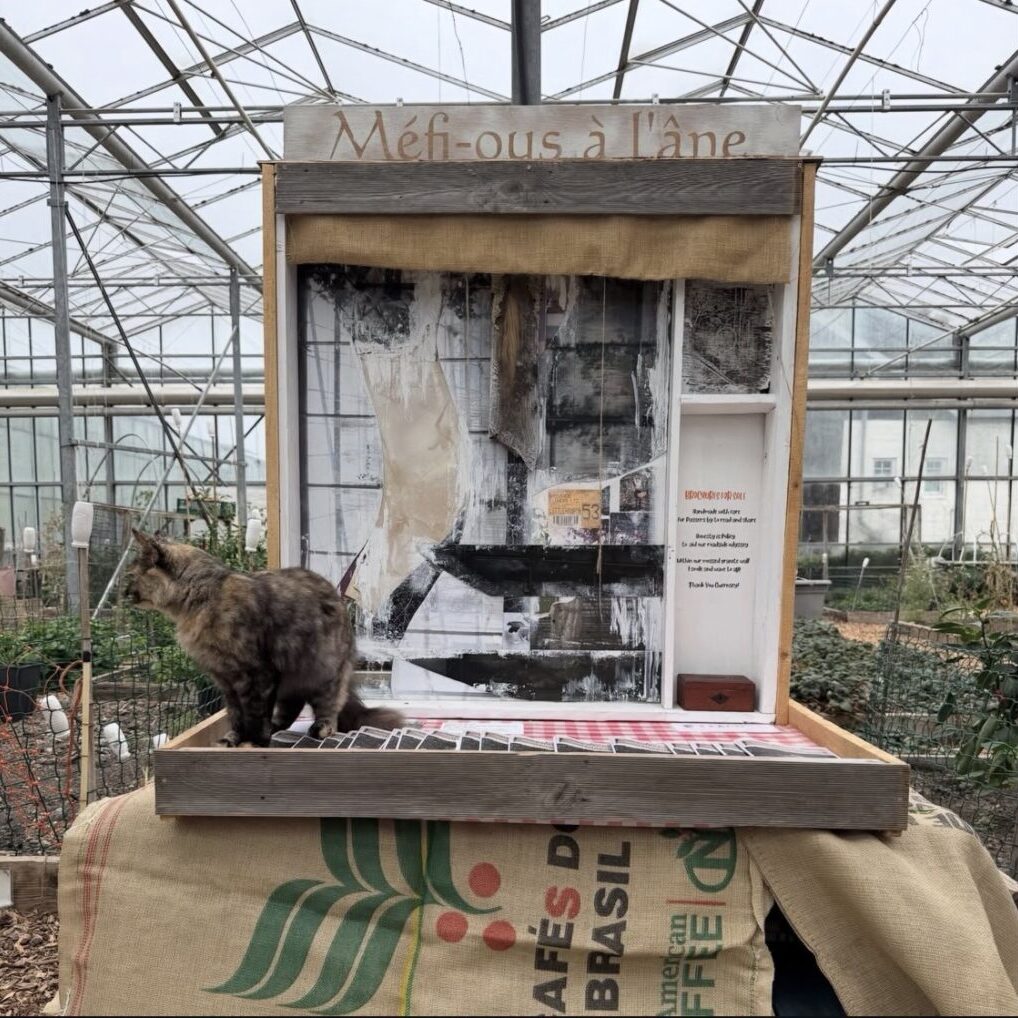 A tortoiseshell longhair cat sits atop a contemporary artwork made from reclaimed materials.